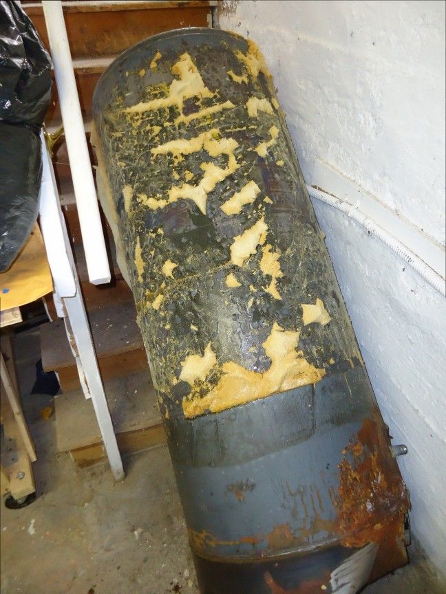 The steel inner tank of a hot-water cylinder with its casing removed, rusted near the base